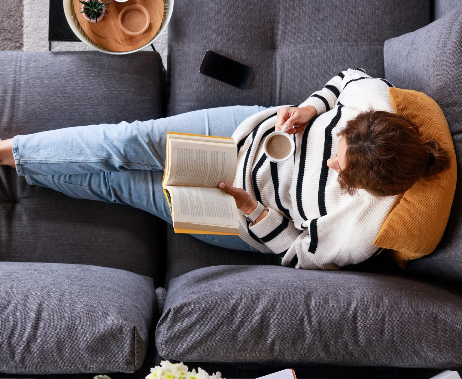 Woman reading book with coffee on couch.
