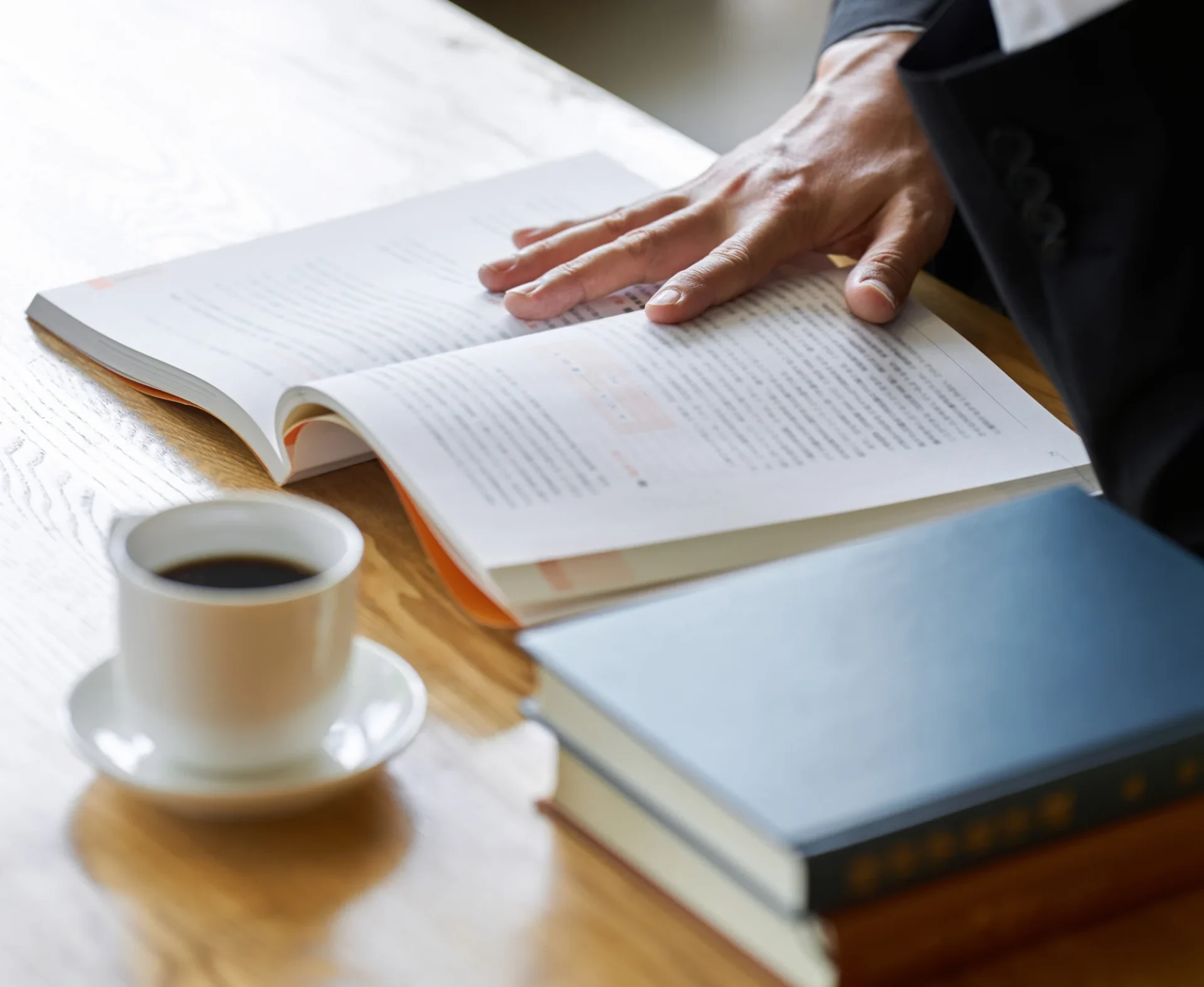 Hand on open book beside coffee cup.