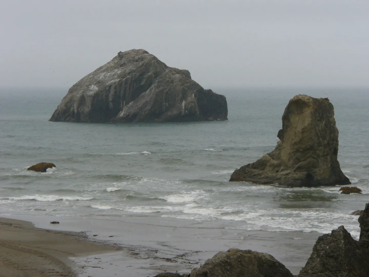 A large rock formation in the ocean near a rocky shoreline.