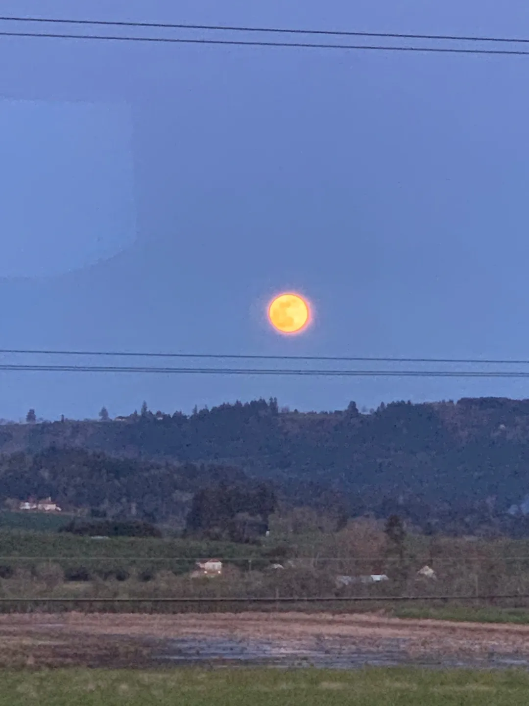 Bright full moon glowing over a hilly landscape at dusk.