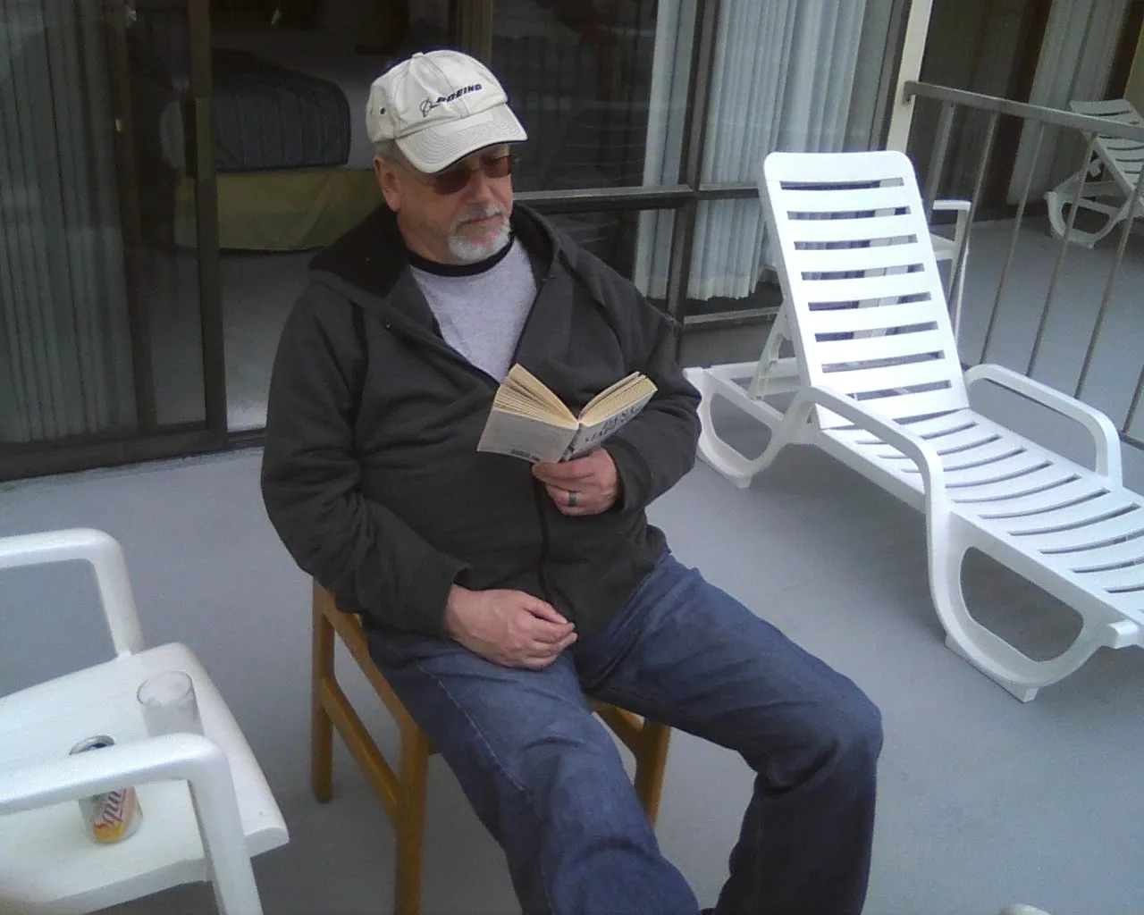 Man reading a book while sitting on a patio chair.